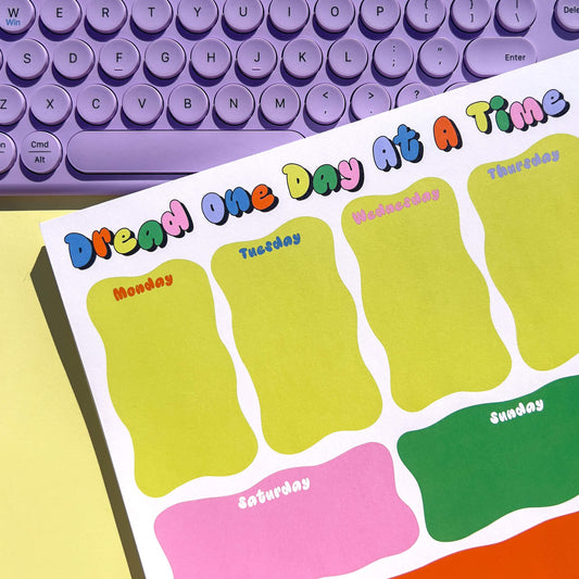 Colorful weekly planner notepad on a desk with a purple keyboard.