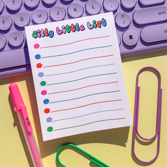 Colorful notepad with 'Silly Little List' on a purple keyboard and stationery items.
