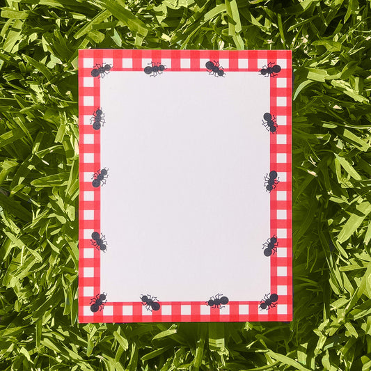 Notepad with red checkered border and ant illustrations on grass