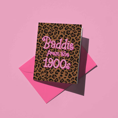 A leopard print greeting card with a bright pink envelope behind it, pink text that reads 'Baddie from the 1900s' against a light pink background.