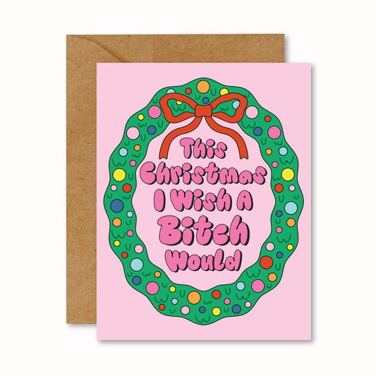 Pink greeting card with green wreath and red bow, featuring playful text, next to a brown envelope on a white background.
