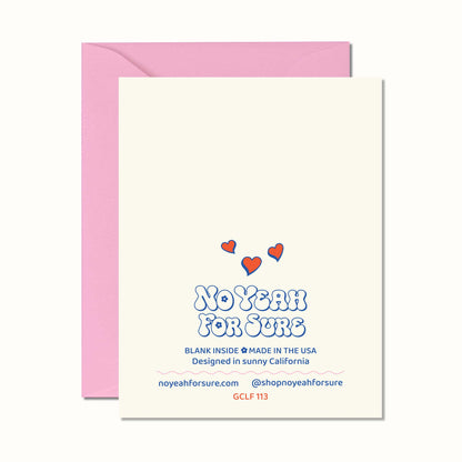 A cream-colored greeting card with a pink envelope behind it. The card features the text 'NO YEAH FOR SURE' in a blue bubbly font, with three small red hearts above it.