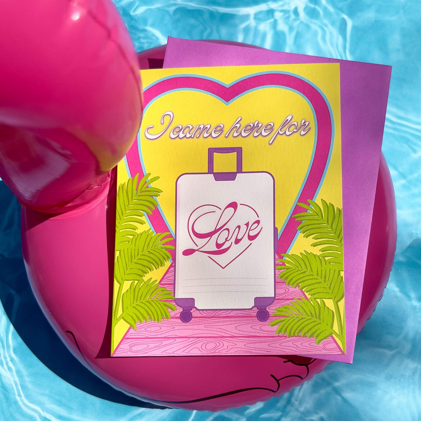 Greeting card with heart design, suitcase illustration, and 'I came here for love' text on a pink inflatable pool ring. 