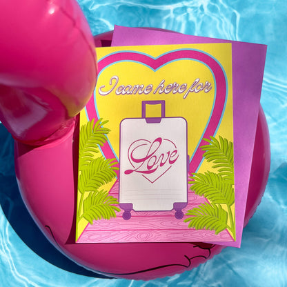 Greeting card with heart design, suitcase illustration, and 'I came here for love' text on a pink inflatable pool ring. 