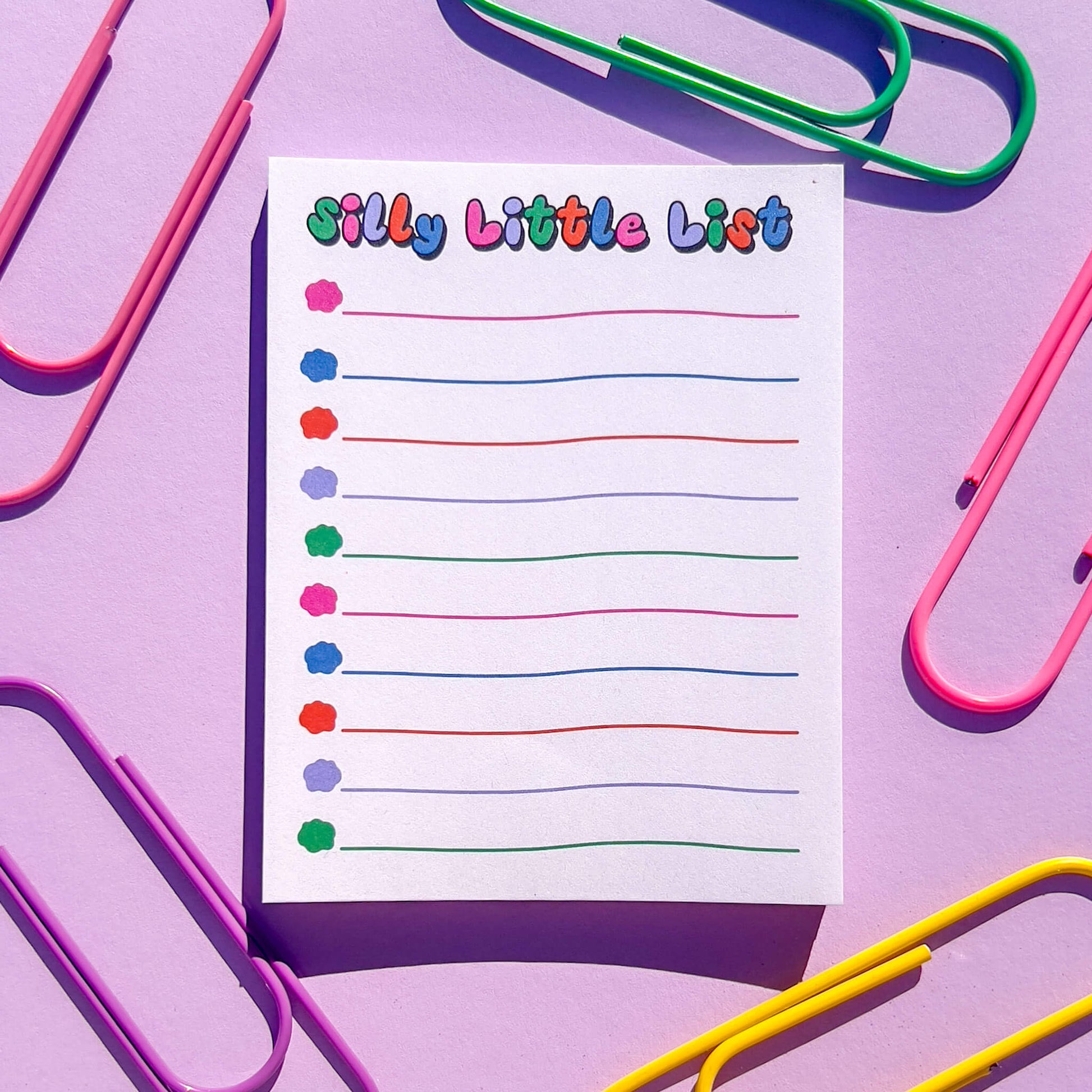 Colorful 'Silly Little List' notepad with paperclips on a purple background