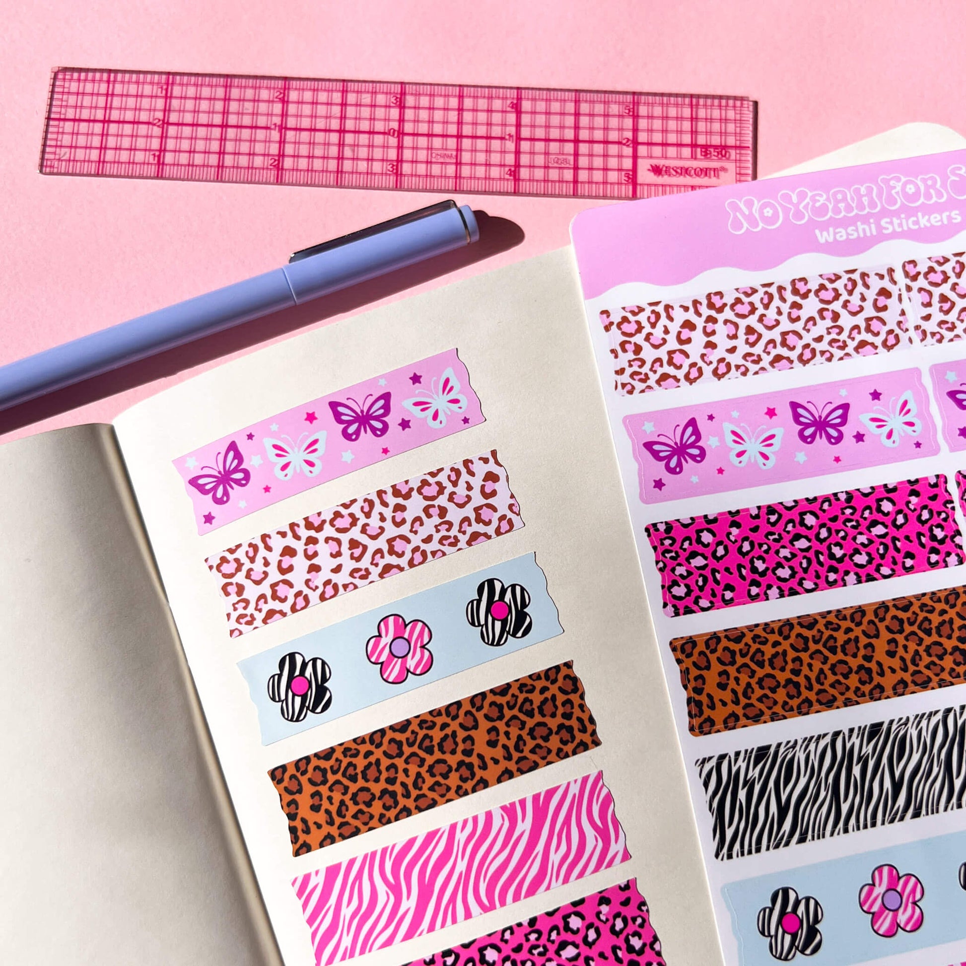 A sheet of washi stickers displayed on an open notebook, alongside a pink ruler and a purple pen. The stickers feature various patterns including leopard print, zebra print, butterflies, and flowers in multiple colorways.