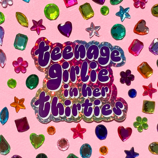 Glitter sticker with text reading 'Teenage Girlie in her Thirties' surrounded by colorful gemstones on a pink background