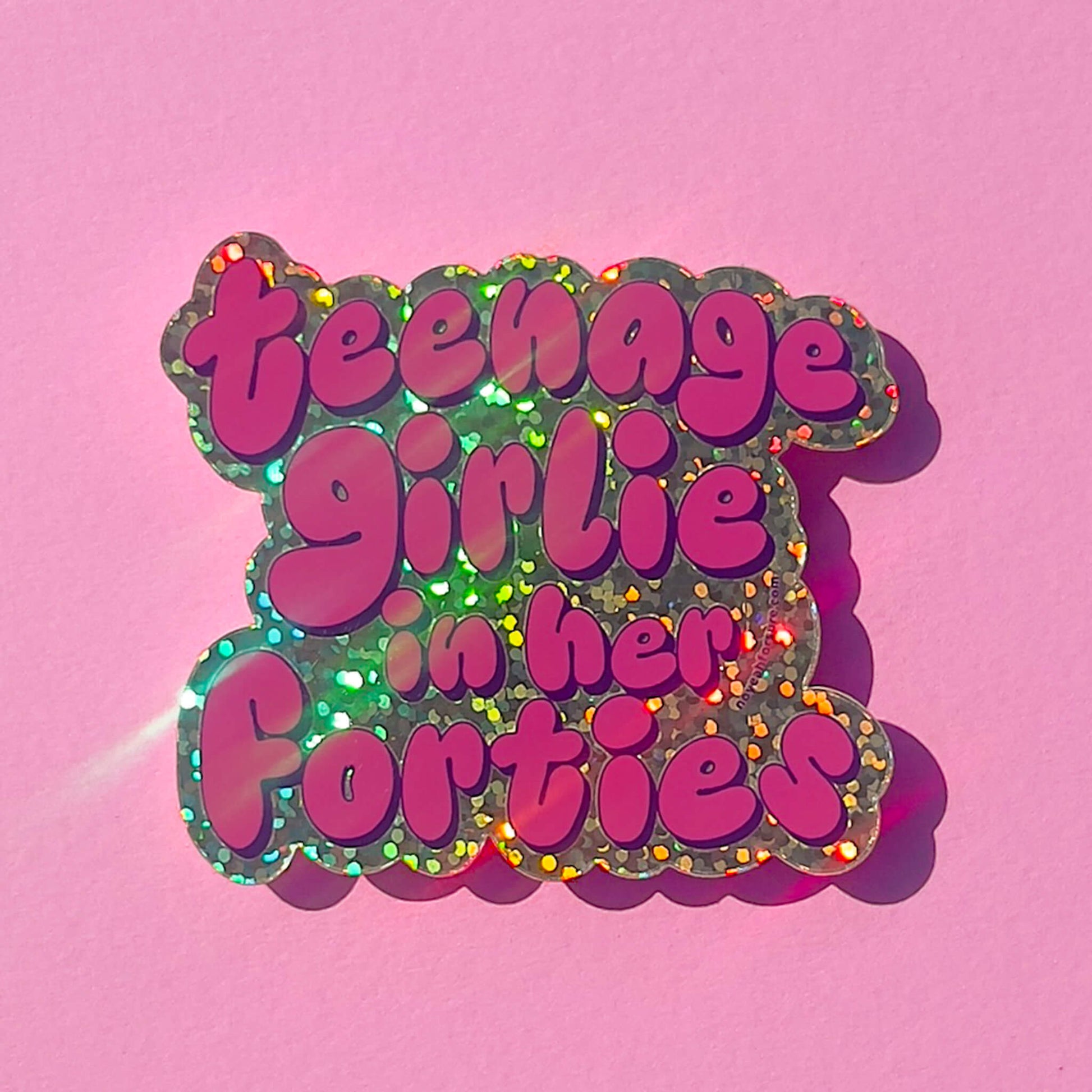 Glitter sticker with 'teenage girlie in her forties' text on a pink background
