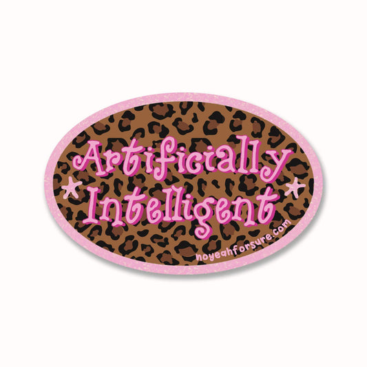 An oval sticker with a pink border and leopard print background, featuring the text 'Artificially Intelligent' in pink cursive with white outlines, and a small website URL at the bottom.